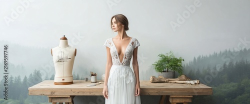Woman in wedding dress stands by table with mannequin, serene forest backdrop