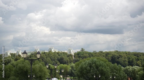 Overcast park avenue with lampposts leading to fountain and distant pale mint turrets above tree ridge, with park, fountain, walkway, lamppost detail, showing lamp, tree, forest, canopy context