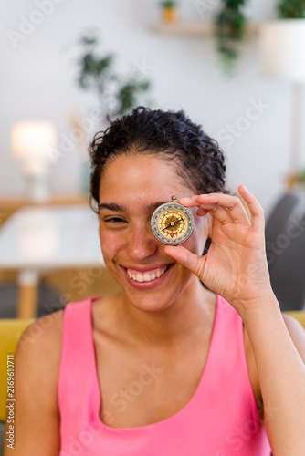 A smiling Hispanic woman holds a compass indoors symbolizing guidance