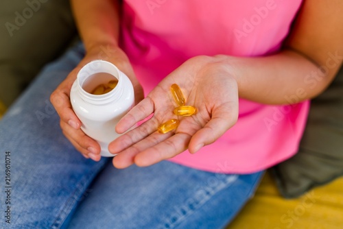 A Hispanic person holds yellow vitamin capsules and a supplement