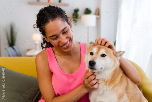 A Hispanic woman smiles while petting a dog indoors