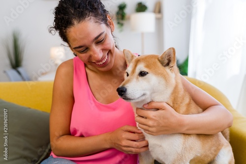 A Hispanic woman affectionately pets her dog in a cozy living room