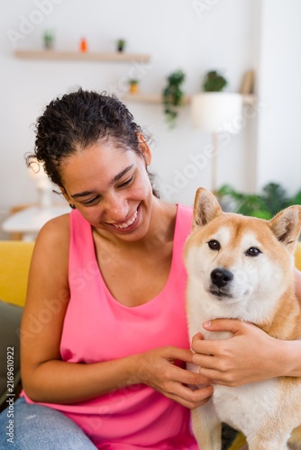 A Hispanic woman happily pets her dog indoors