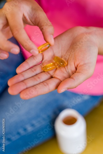 Hispanic Person holding yellow softgel pills with pill bottle