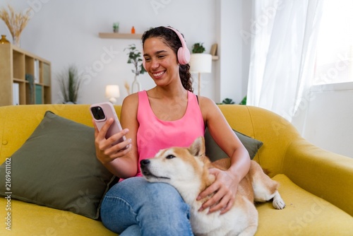 A Hispanic woman listens to music and pets her dog on a yellow couch
