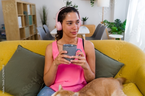 A Hispanic woman relaxes on a yellow couch listening to music