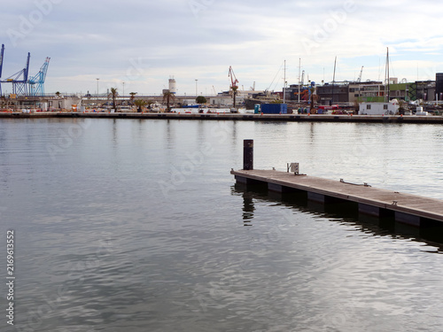 Empty wooden pier in calm harbor water with distant view of industrial cargo port cranes and docks. concept for global maritime logistics reports, maritime transport banners or travel agency websites