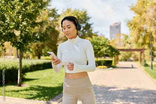 A young beautiful Asian woman listens to music while walking in a sunny green park.