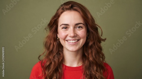 Smiling young woman with red hair posing for a portrait against a green background
