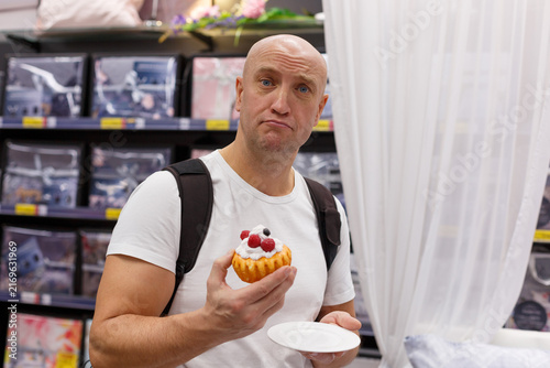 Photography Mature caucasian man makes a skeptical unhappy face while holding a cake, doubt and disappointed reaction for food choice, diet and emotion content