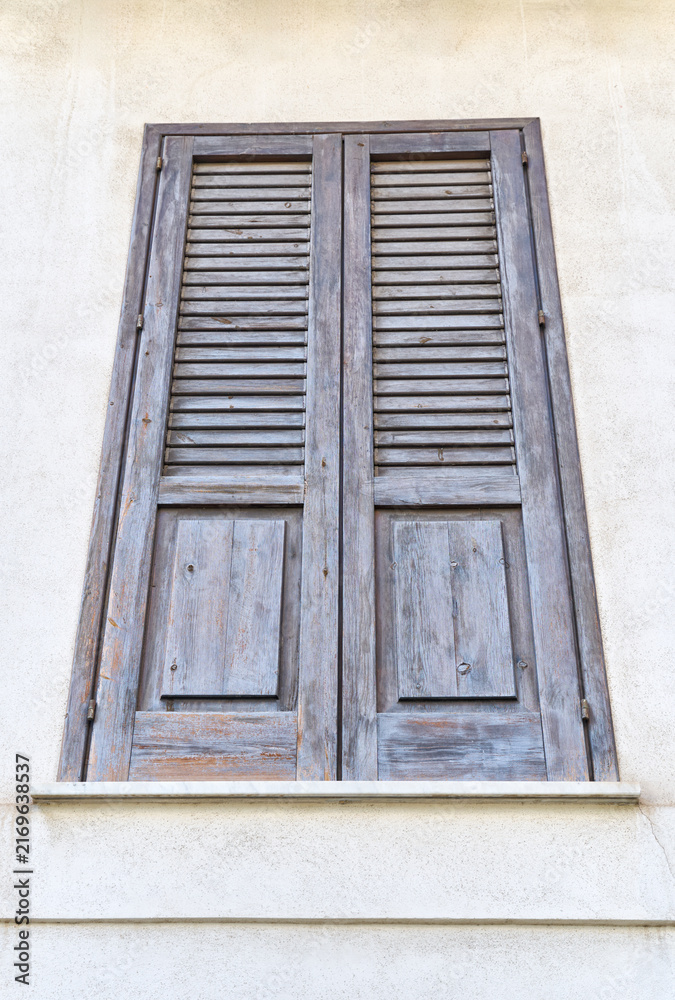Fototapeta premium Closed dark brown wooden shutters on a traditional Mediterranean building facade in Sicily, Italy, showing rustic architecture, aged texture and classic louvered design.