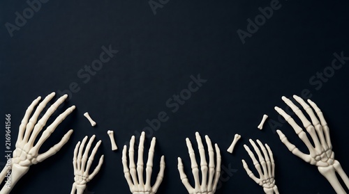 Multiple human skeleton hands reaching up from the bottom against a dark black background for halloween