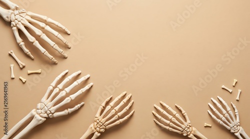 Minimalist flat lay featuring white skeleton hands and small bones arranged around the edges of a light beige background as a seasonal decorative frame