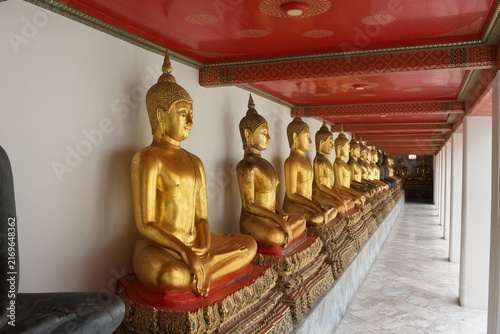 Fotografie vanishing perspective of seated golden buddha statues lining the marble cloister