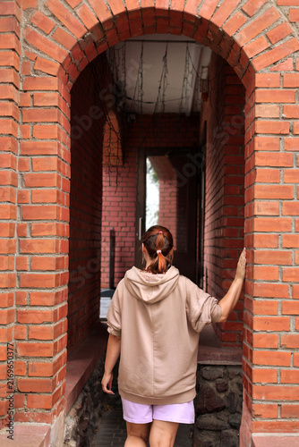 фотографія Rear view of a woman in a beige hoodie touching a red brick archway in an old ur