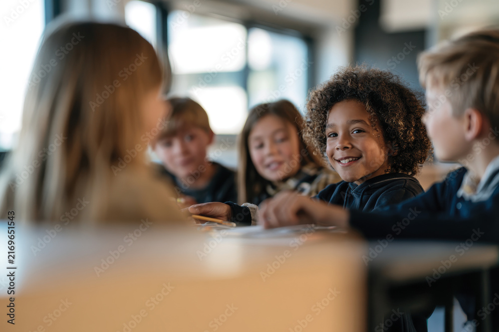 Fototapeta premium A group of smiling children engages joyfully in educational activities, showcasing friendship and collaboration in a bright classroom setting filled with natural light.