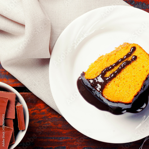 Slice of Brazilian carrot cake with glossy chocolate frosting on a white plate on a white tablecloth.
