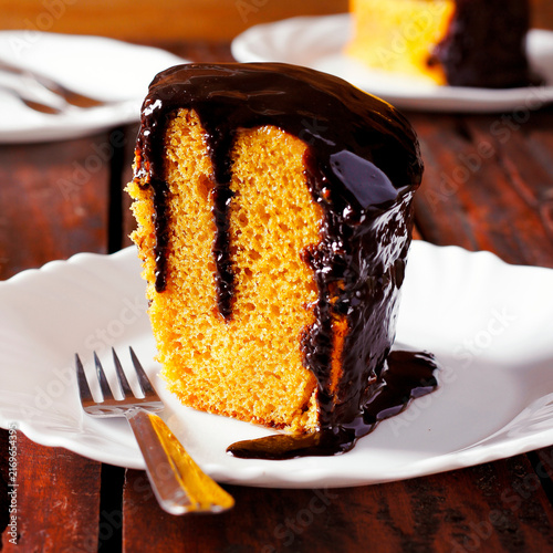 Slice of carrot cake with chocolate, accompanied by other portions on white plates.