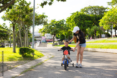 Mother helping young child ride bicycle on path