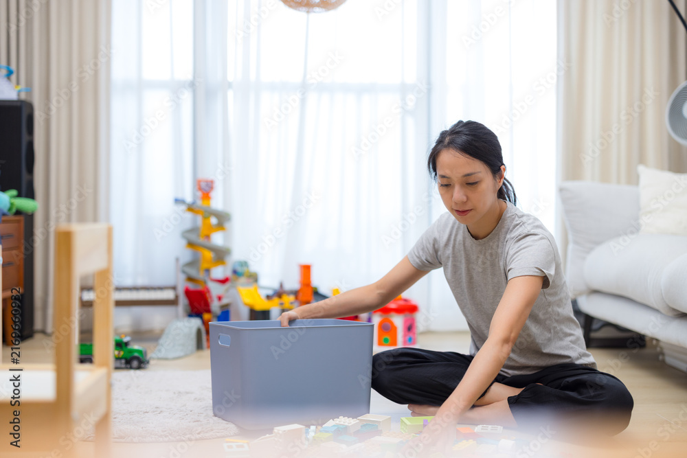 Obraz premium Woman sitting on floor packing toys into grey storage box