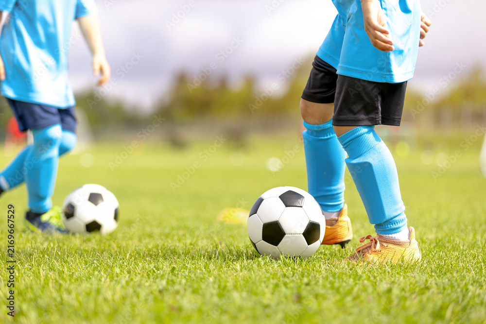 Fototapeta premium Close-Up of Junior Soccer Players in Light Blue Kits Dribbling Soccer Balls - Youth Football Training Drill and Ball Control Practice on Grass