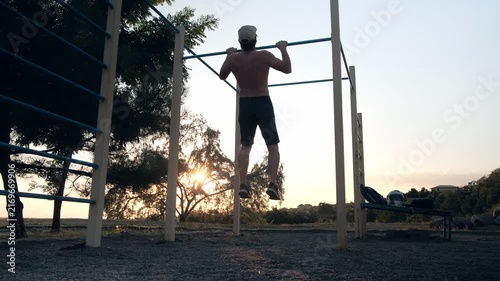 Middle Aged Man Doing Pull Ups On Sports Area. View from below, from the back. 