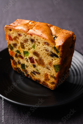 Delicious fruit cake with dried fruits served on a black plate, dark minimalist background