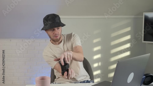 an energetic musician performs with a guitar in a modern indoor setting with light patterns on the wall, wearing a white shirt and hat, posing and raising arms.
