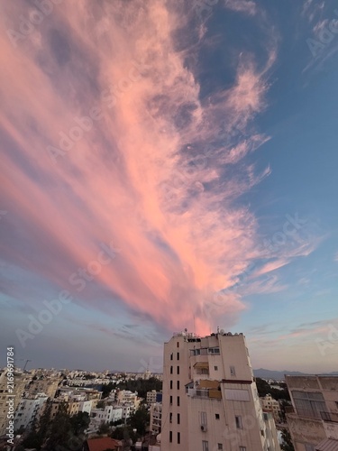 Cuadro en lienzo Pink cirrus clouds streaking across the sky above apartment buildings at sunset