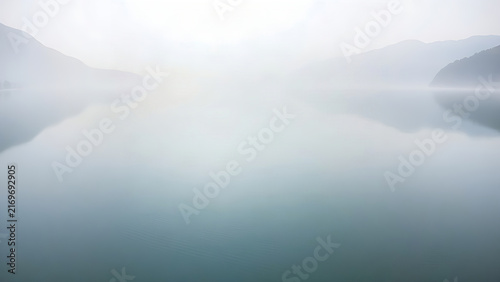 A calm mountain lake with a gentle slope of water, misty morning, mirror-like surface.