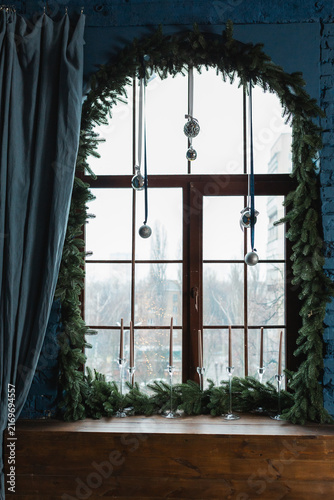 Decorated arched window with green pine garland candles and silver hanging ornaments.