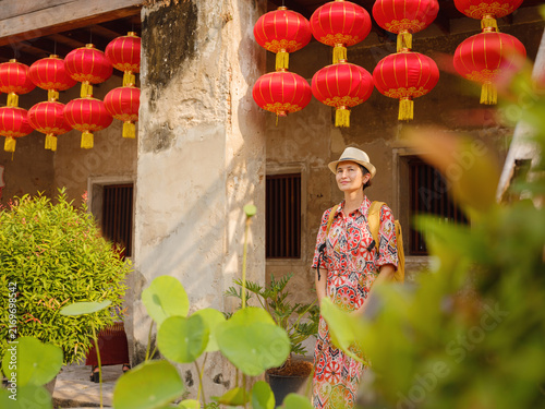 Beautiful female traveler poses next to vibrant hanging red Chinese lanterns in Lhong 1919 Bangkok during traditional Lunar New Year celebration. Festive decorations create warm cultural backdrop.