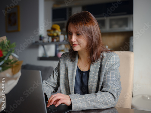 Mother working remotely from home, multitasking between professional tasks and family responsibilities, using a laptop in a cozy home environment.
