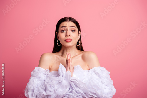 Obraz na plátně Young woman pleading with hands together in a prayerful pose against a pink back