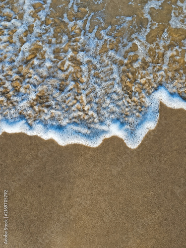 Фотография Top view of white sea foam wave on wet sandy beach with copy space
