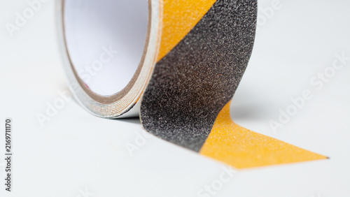 Fotografie Black and yellow industrial anti-slip safety tape in a roll, featuring diagonal warning stripes for marking hazardous areas and improving workplace floor traction