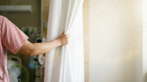 Medical staff hand pulling privacy curtain open in bright hospital room, symbolizing patient care and healthcare services.