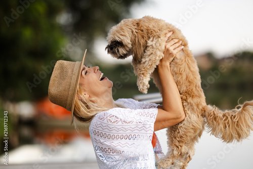 Woman Enjoys Summer by the River While Holding Her Dog and Smiling With Joy