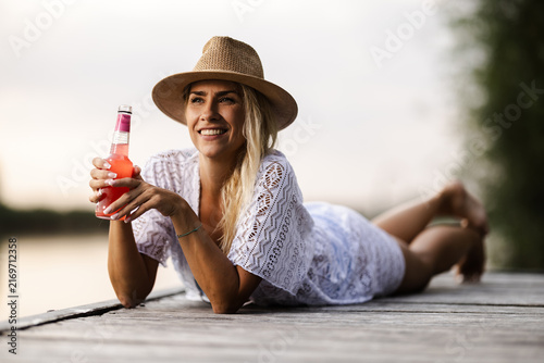 Woman Enjoys Drink by the River on a Summer Day While Lying on a Dock