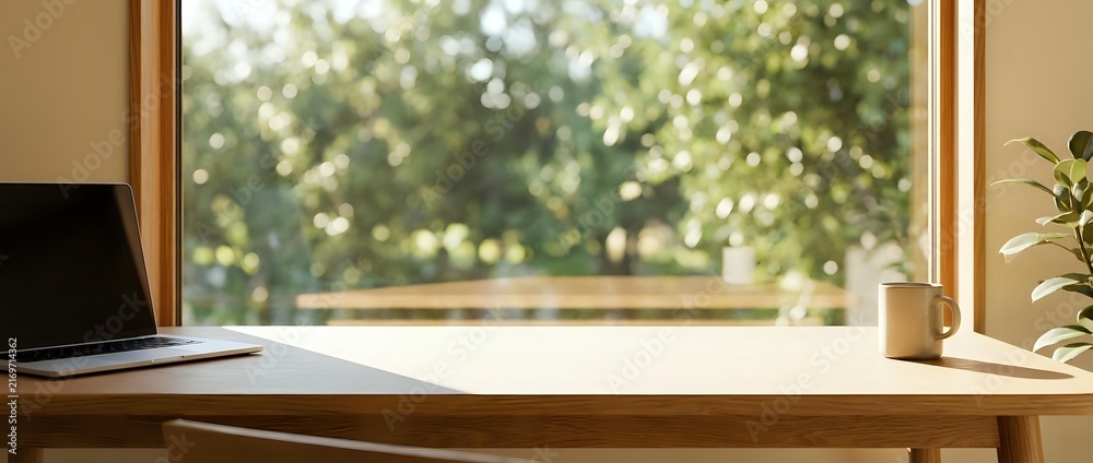 Obraz premium Wooden desk with laptop and plant near window overlooking blurred