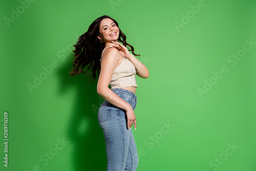 Bild auf Leinwand Smiling young woman in casual jeans and crop top posing against a bright green b