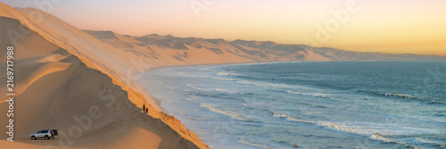 Tourists in the sand dunes and ocean view in Sandwich Harbour, Namib Naukluft Natural Park panoramic landscape in Namibia, Africa web banner
