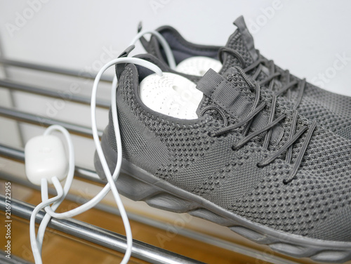 Electric shoes dryer close up. Pair of grey wet sneakers drying with a plug-in boot warmer on a shoe rack. The concept of household technologies and smart gadgets.