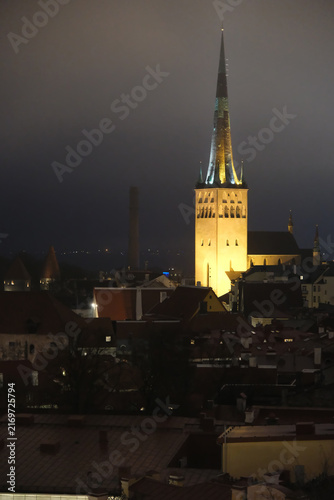 illuminated St. Olaf's Church spire and Old Town roofs at night in Tallinn, Estonia.