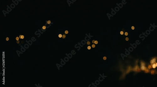 Blurred golden bokeh lights on dark background, creating festive atmospheric illumination for abstract holiday celebrations and elegant design overlays.