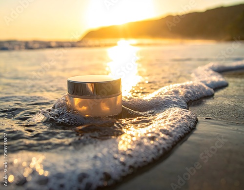 A jar of cosmetic cream sits serenely on a wet sandy beach, embraced by gentle ocean waves and illuminated by the warm, golden light of the setting sun.