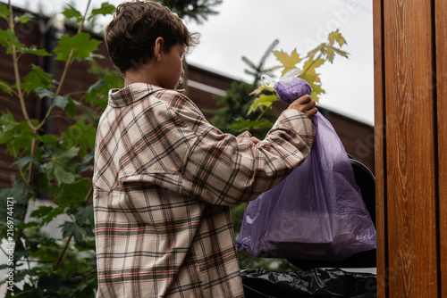 Obraz na plátne Man throws a purple garbage bag into a street trash bin, promoting cleanliness and responsibility