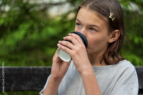 Принти на полотні Young girl sipping from a paper cup while sitting outdoors