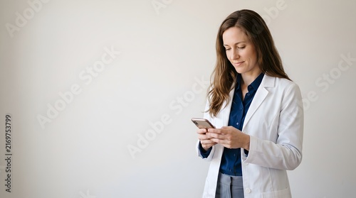 Female doctor in white lab coat typing text message on smartphone against white background with mobile phone using phone hospital staff