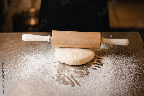 Фотография Chef Using Wooden Rolling Pin to Flatten Dough Ball on Table